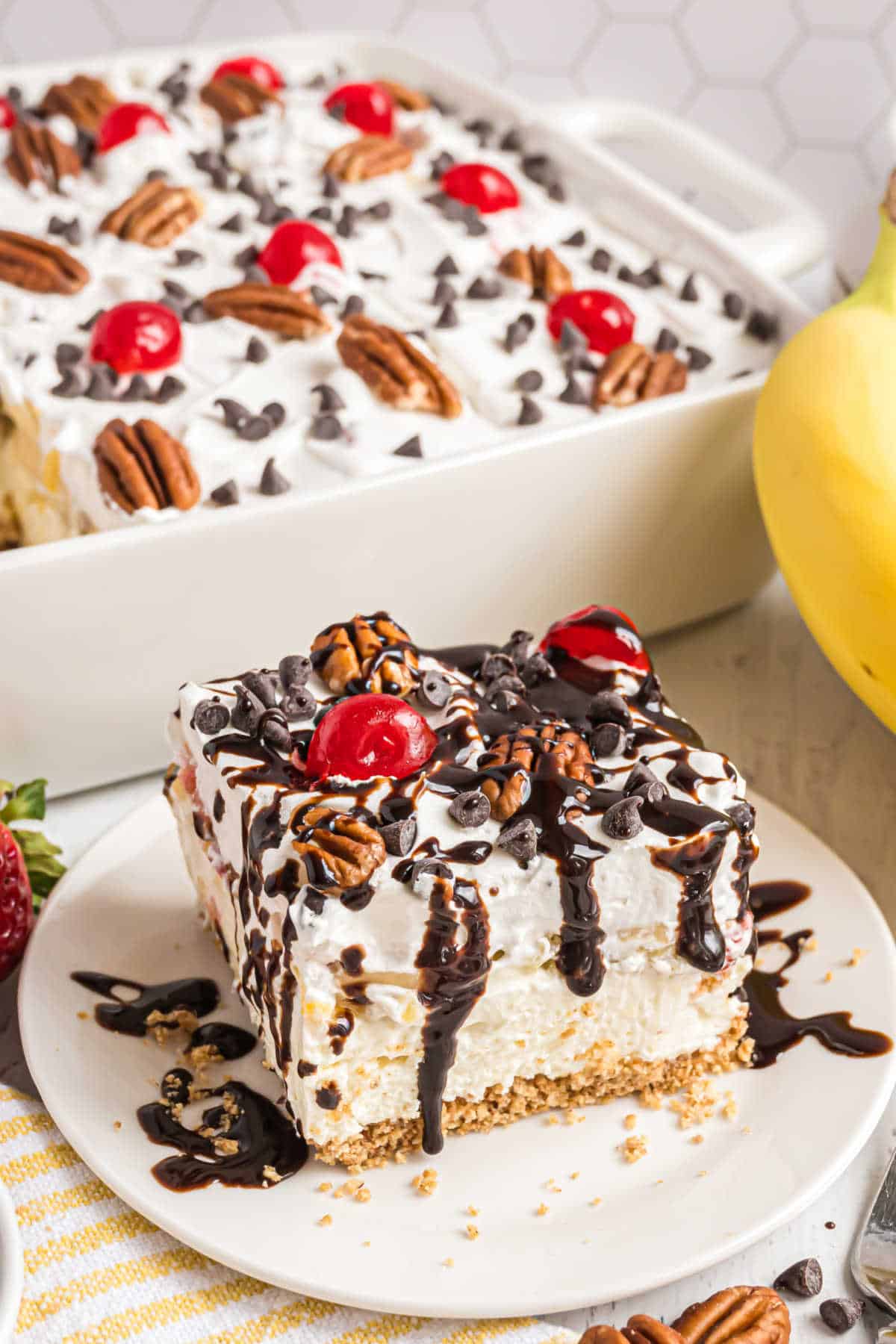 Slice of banana split dessert drizzled with chocolate syrup.