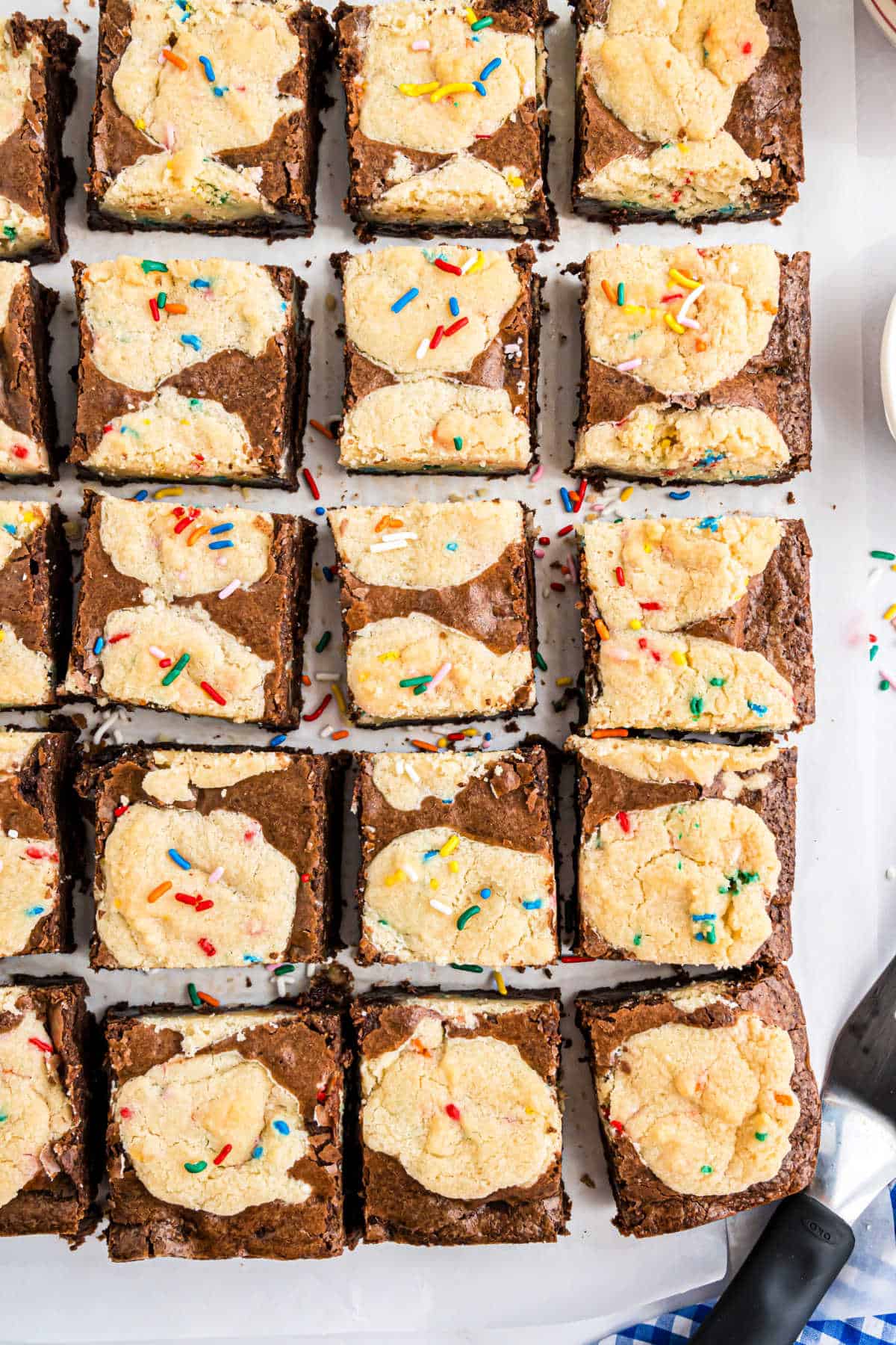 Top view of delicious sugar brookies with cream cheese swirls and colorful sprinkles, sliced atop parchment paper.