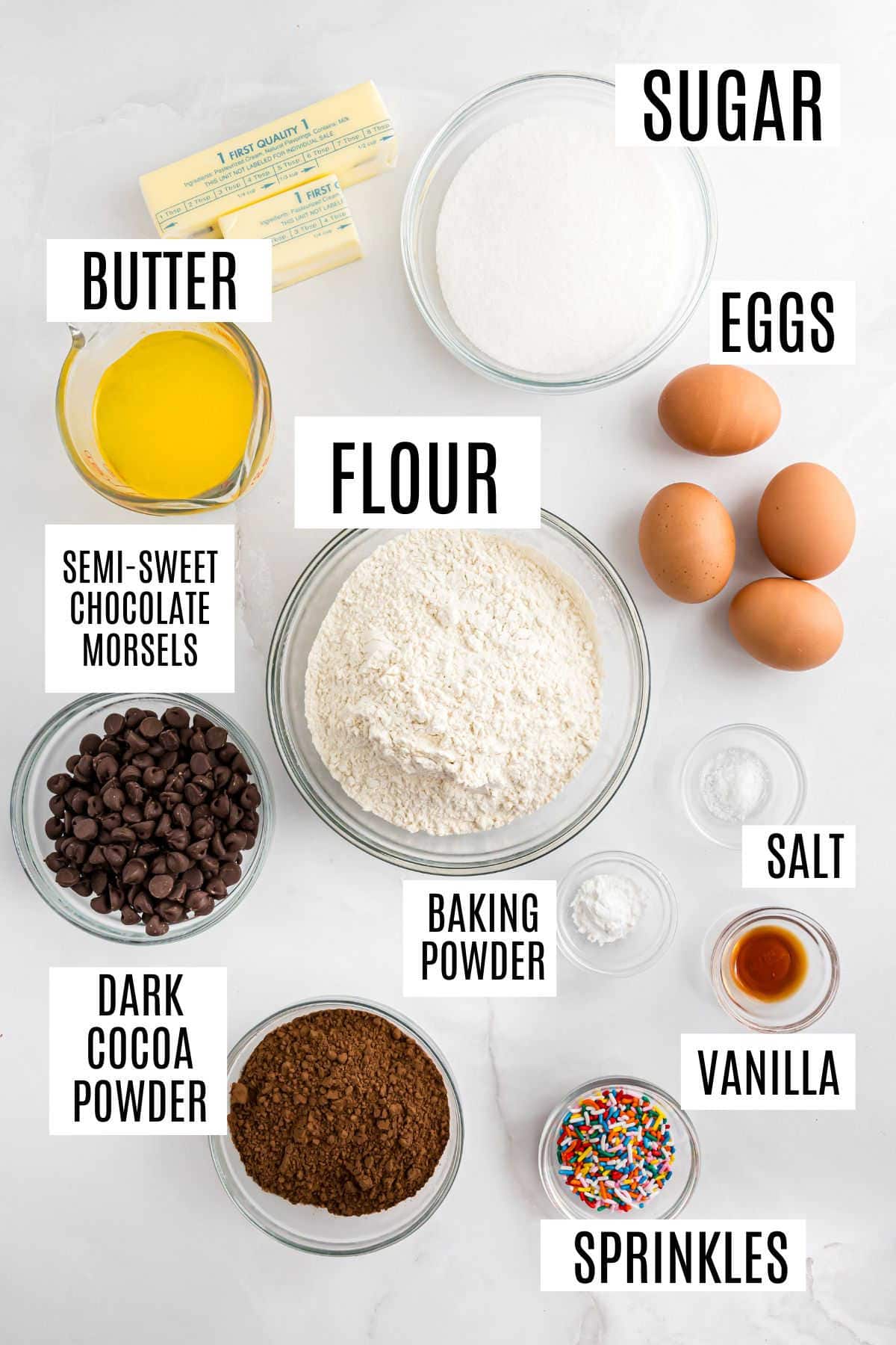 Bowls of baking ingredients labeled: sugar brookies, eggs, butter, flour, chocolate chips, cocoa, salt, vanilla, sprinkles.