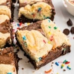 A sugar brookie topped with cookie dough and colorful sprinkles, cut into a perfect square on parchment paper.