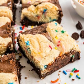 A sugar brookie topped with cookie dough and colorful sprinkles, cut into a perfect square on parchment paper.