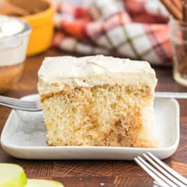 Slice of cake with apples and whipped topping on a white plate.