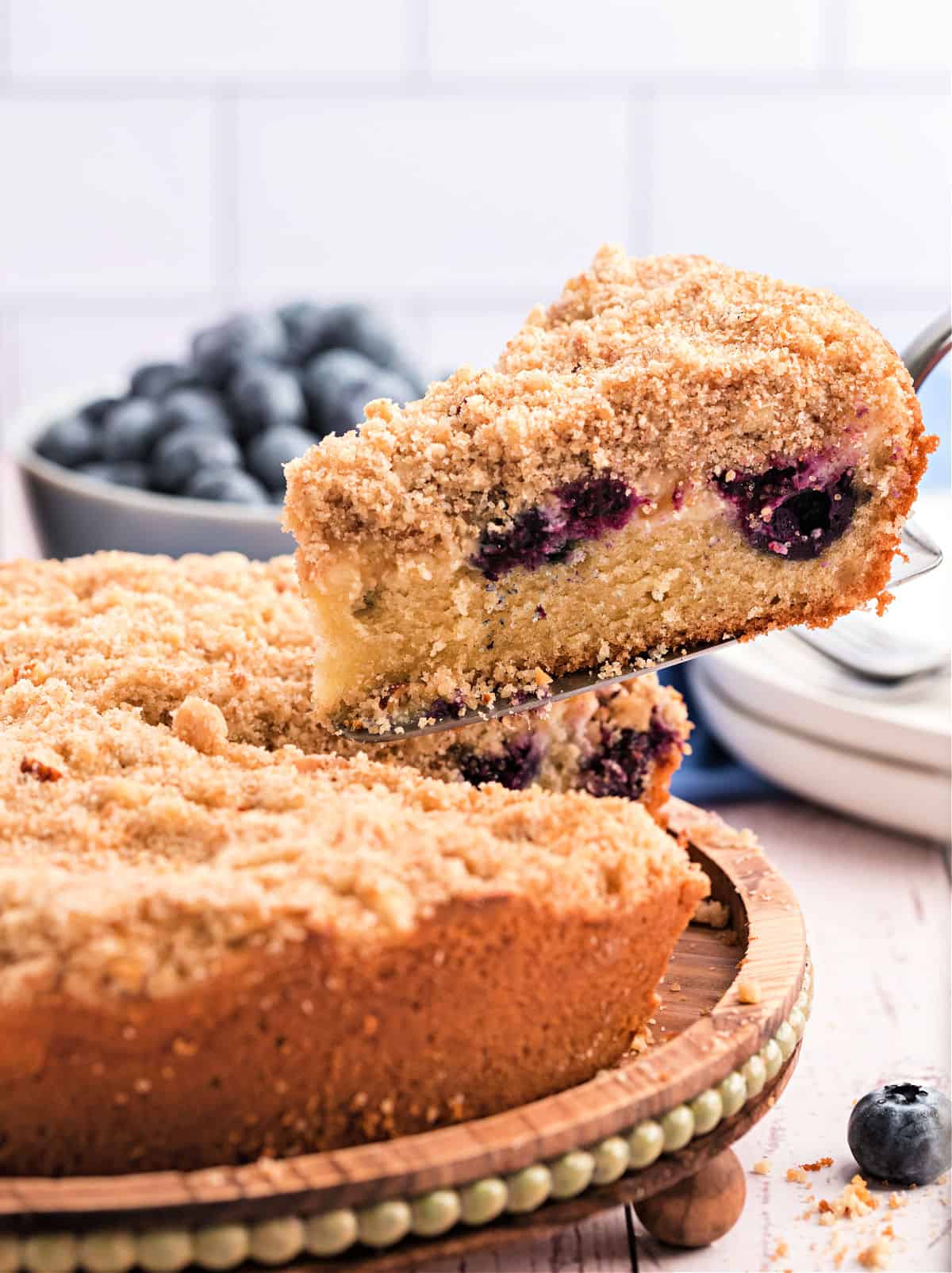 Slice of blueberry coffee cake being lifted off of cake platter.