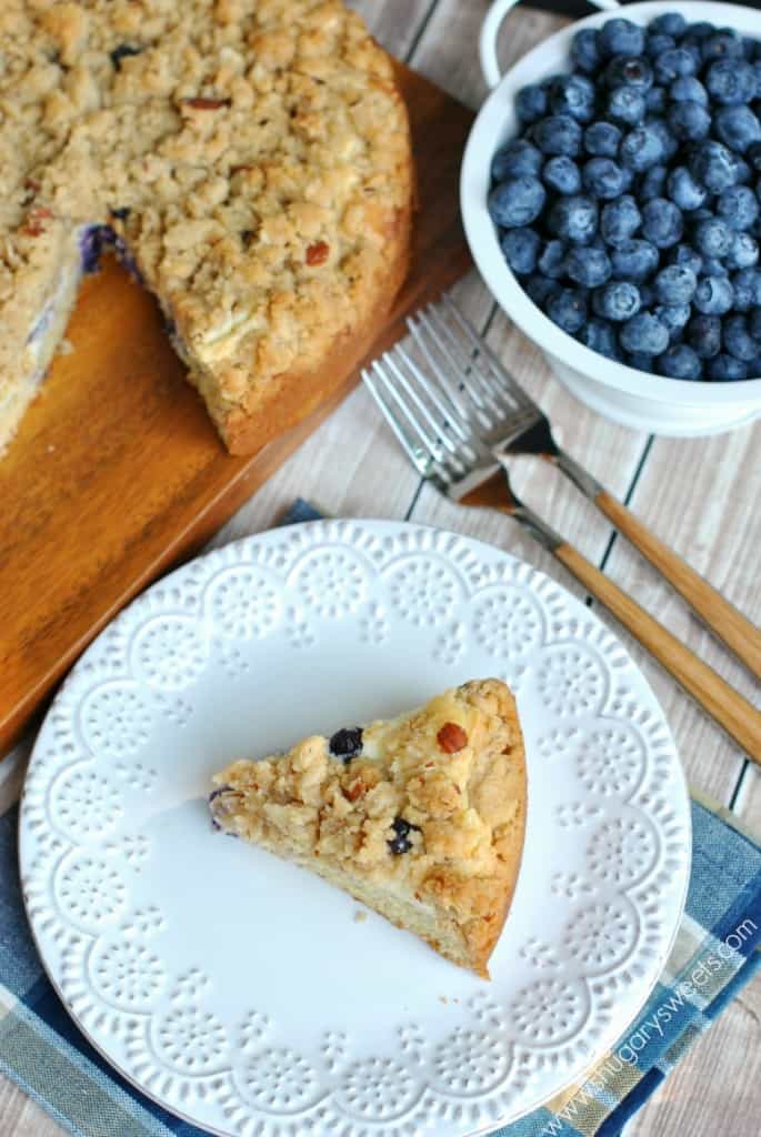 Blueberry coffee cake on white plate with bowl of fresh blueberries.