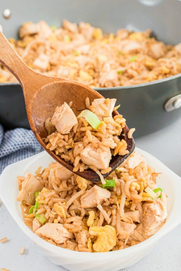 Chicken fried rice being spooned into a white bowl with a wooden spoon.
