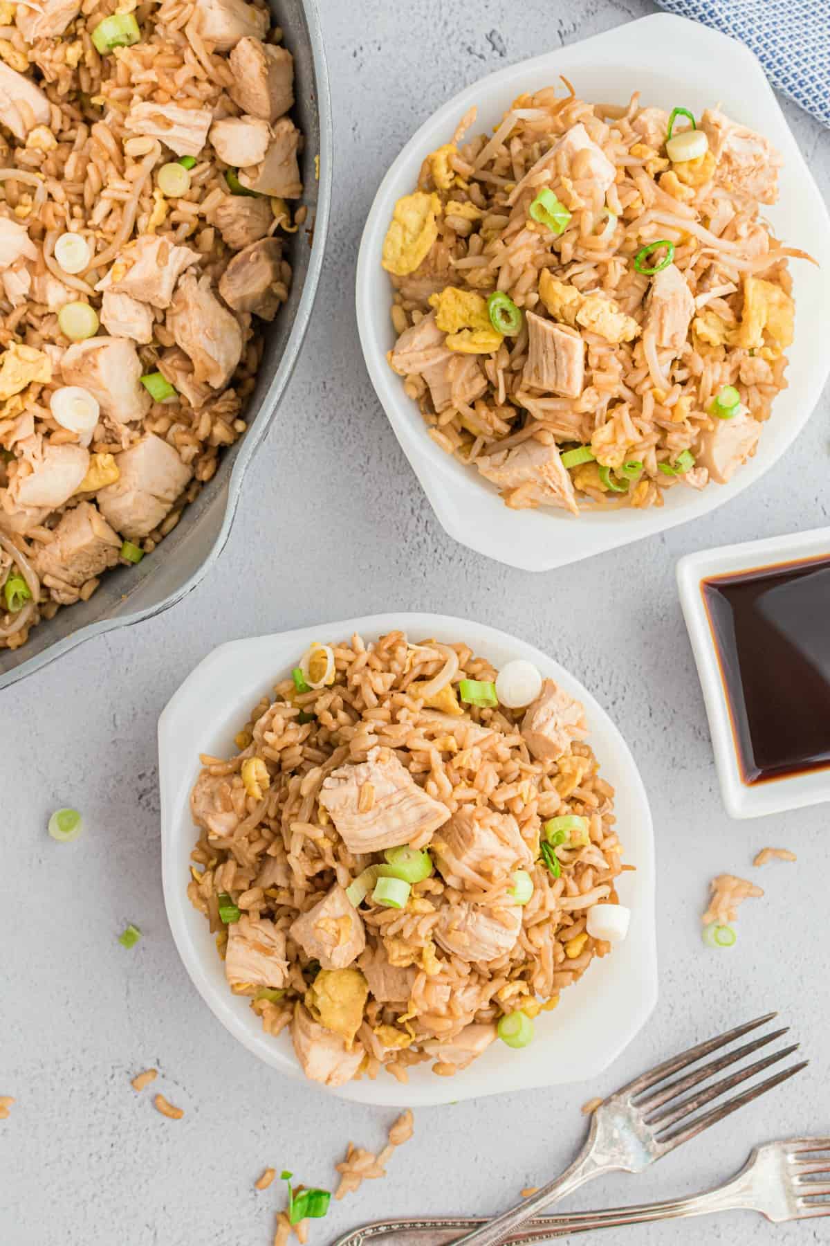 Chicken fried rice served in two white bowls with a side of soy sauce.