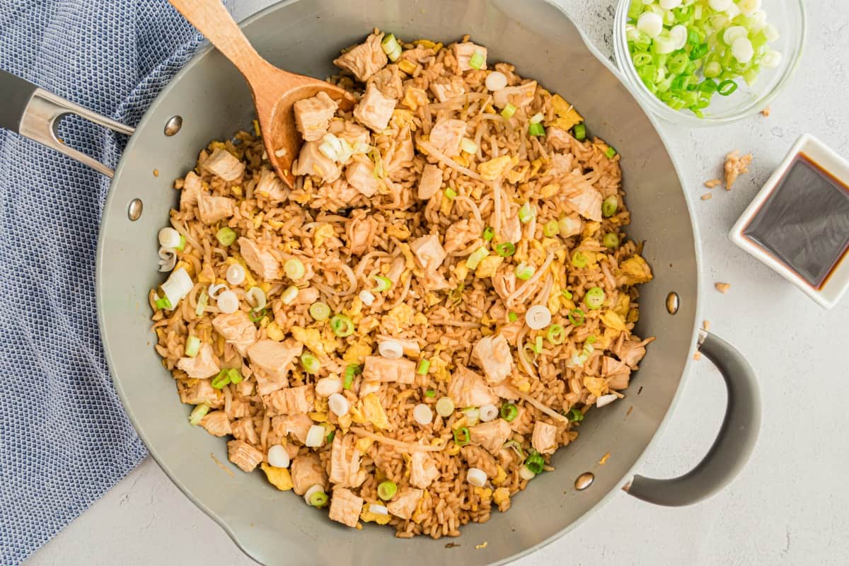 Chicken fried rice in a skillet with a wooden spoon for serving.
