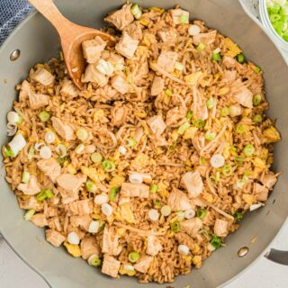 Chicken fried rice in a skillet with a wooden spoon.