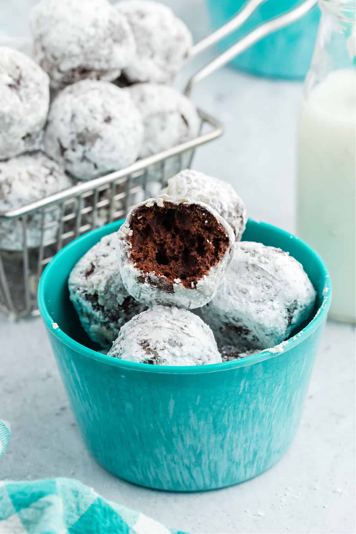 Chocolate powdered sugar donut holes in a teal bowl.