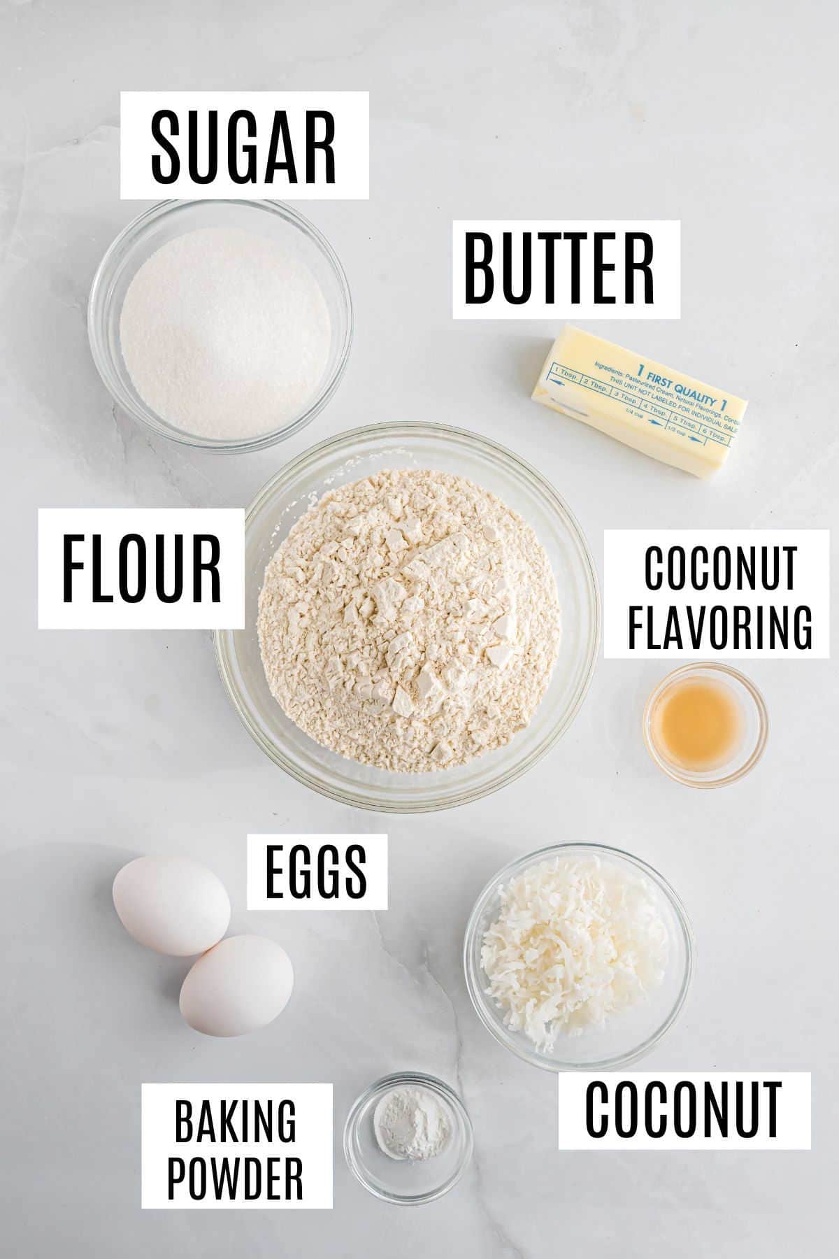 Baking ingredients on a white surface: sugar, butter, flour, coconut flavoring, eggs, baking powder, and coconut—everything you need to make delicious coconut biscotti.