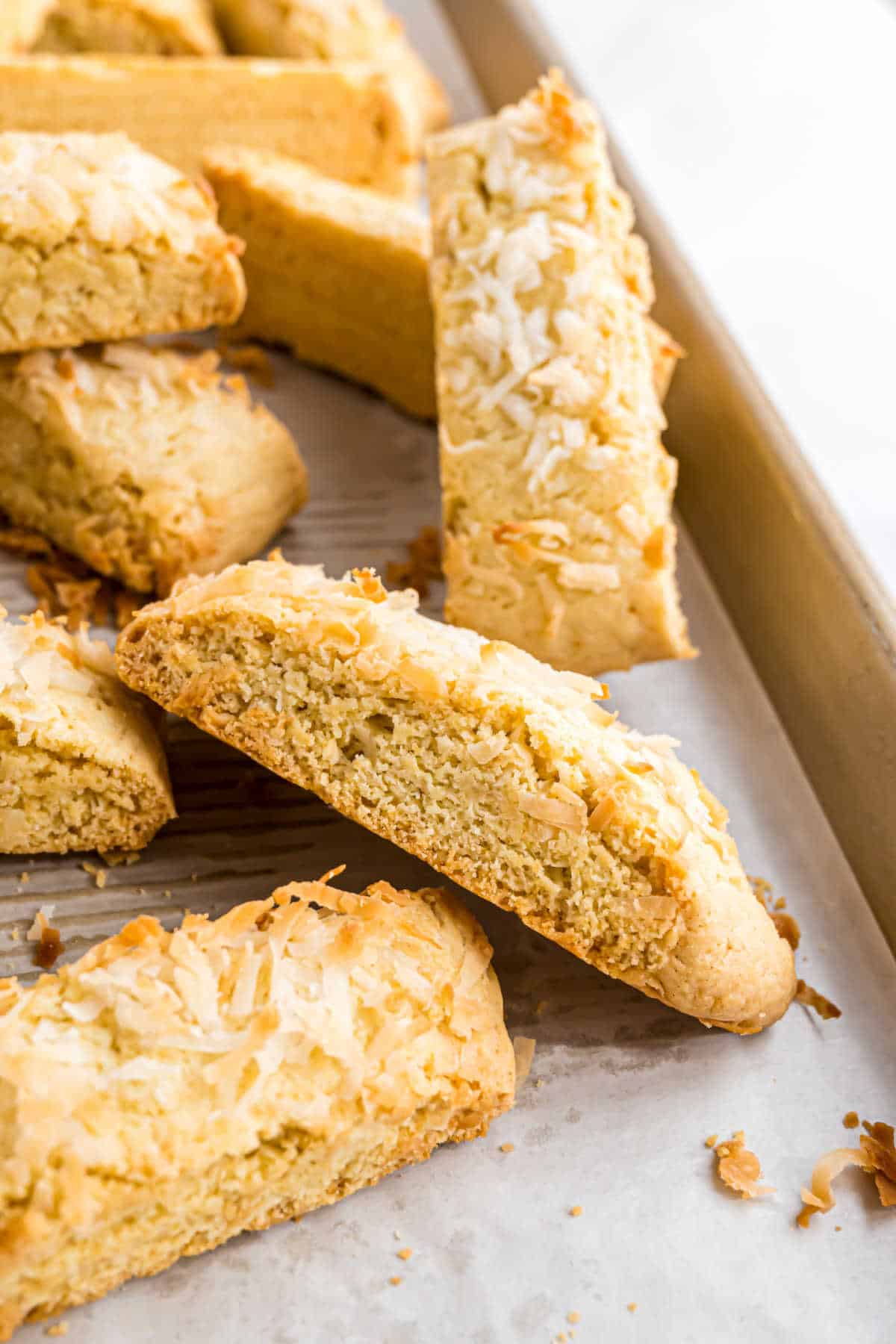 A stack of coconut biscotti is arranged on a parchment-lined baking sheet, showcasing the crisp texture and golden edges of these delightful treats.