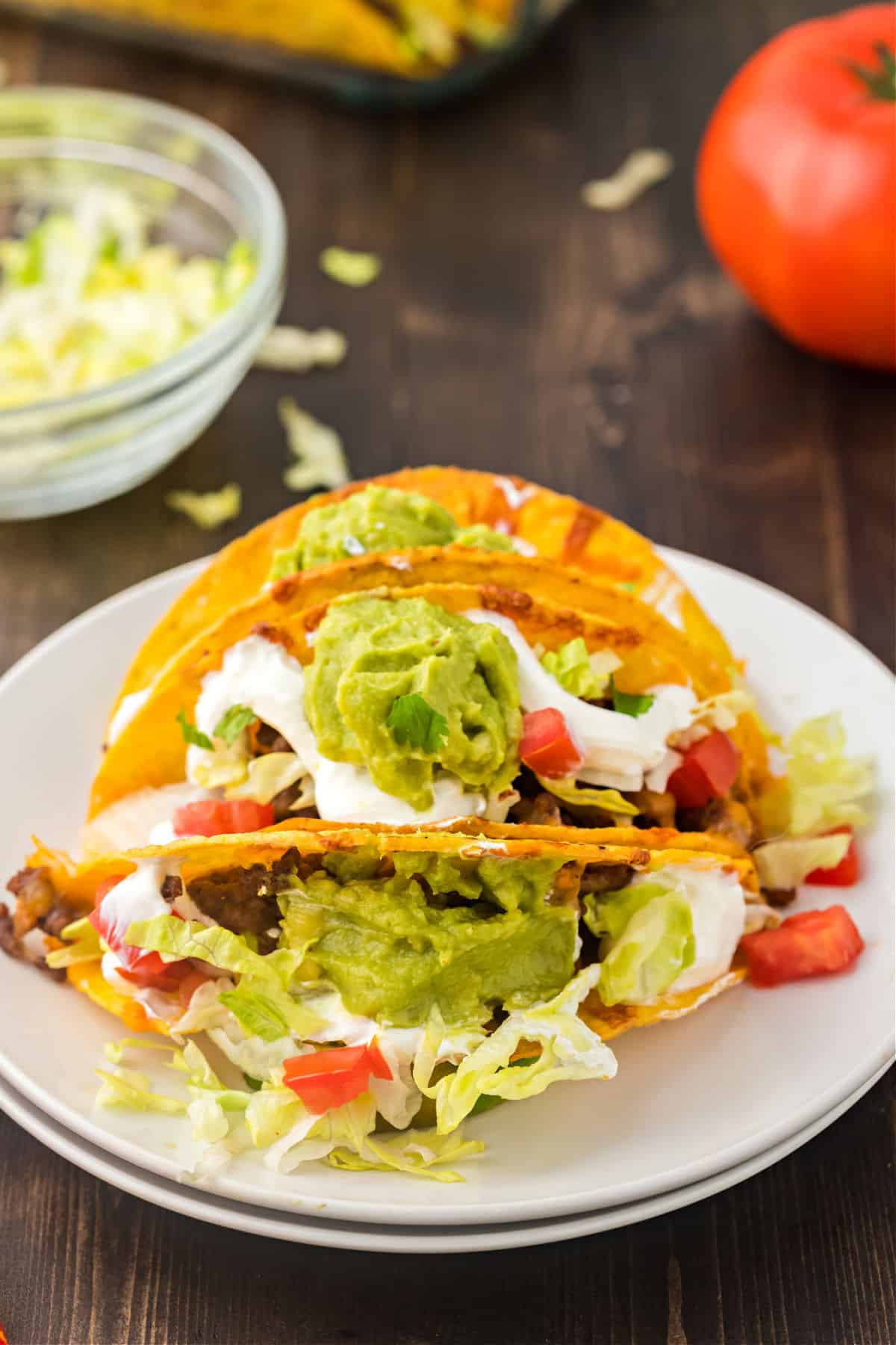 Baked tacos served on a white plate with lettuce, tomato, sour cream, and guacamole.