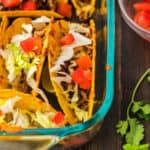 Baked tacos in clear glass baking dish and garnished with vegetables.