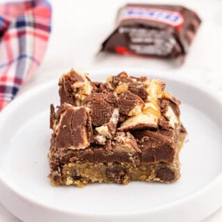 Slice of chocolate chip snickers cookie bar on a white plate.