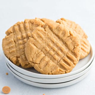 Peanut butter cookies with criss cross pattern on a stack of white plates.