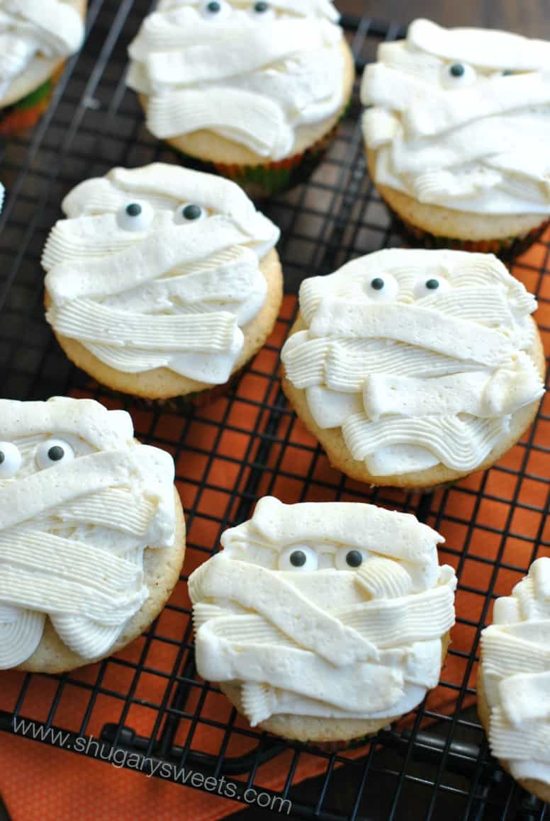 Wire rack with vanilla cupcakes and mummy frosting with candy eyes.