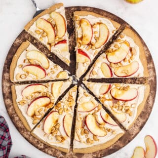Serve pizza for dessert tonight! This Caramel Apple Sugar Cookie Pizza features juicy apples and chopped nuts baked on a soft cookie crust with caramel cheesecake topping. Drizzled with caramel, it's the perfect easy dessert for fall.