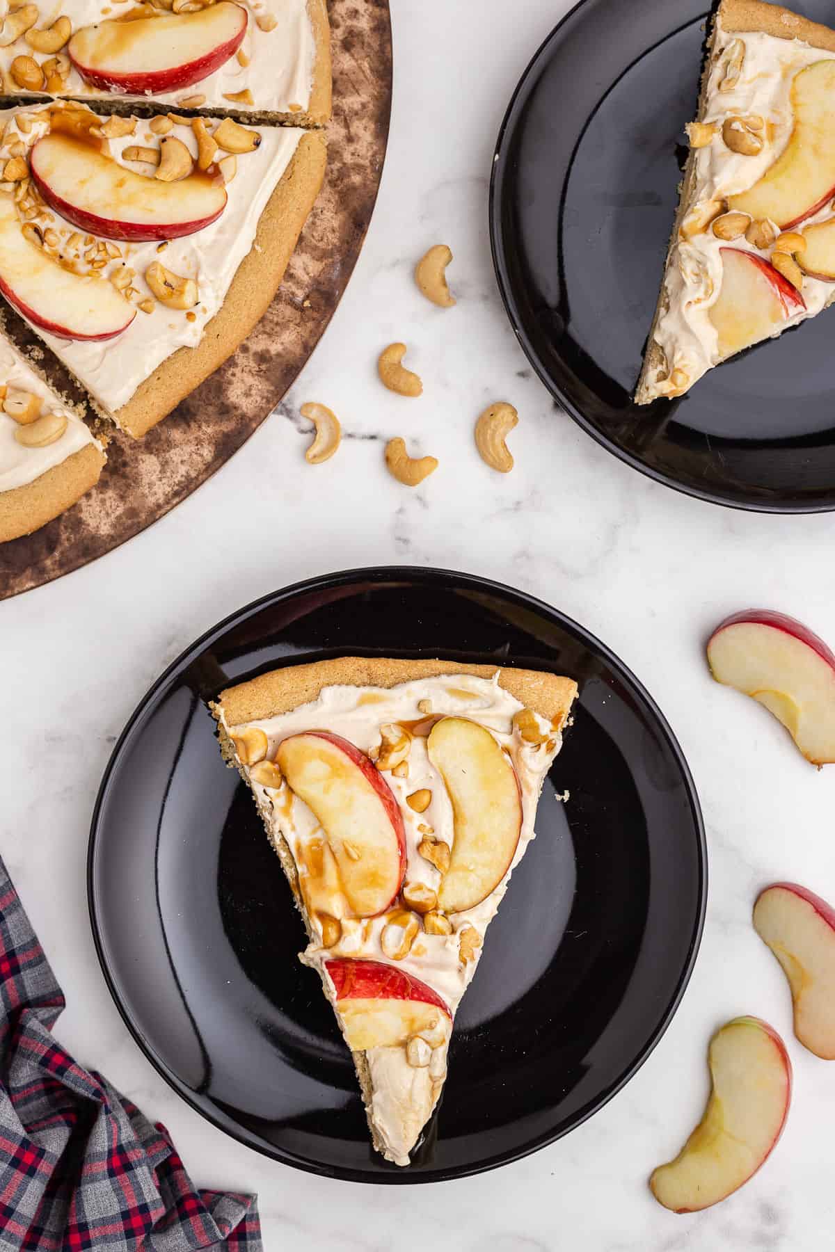 Slice of caramel apple sugar cookie pizza on a black plate.