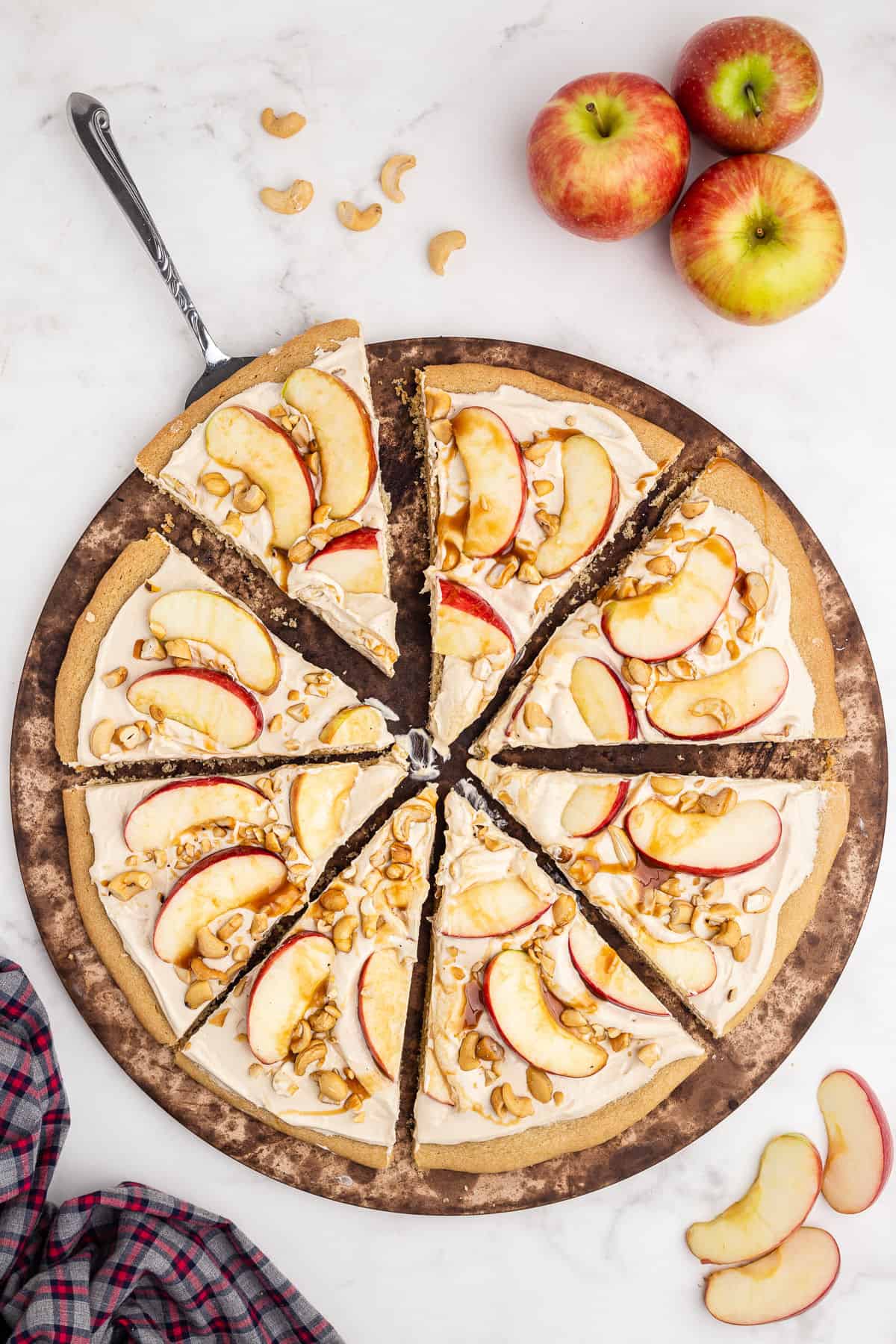 Sugar cookie pizza sliced with apples and caramel sauce.