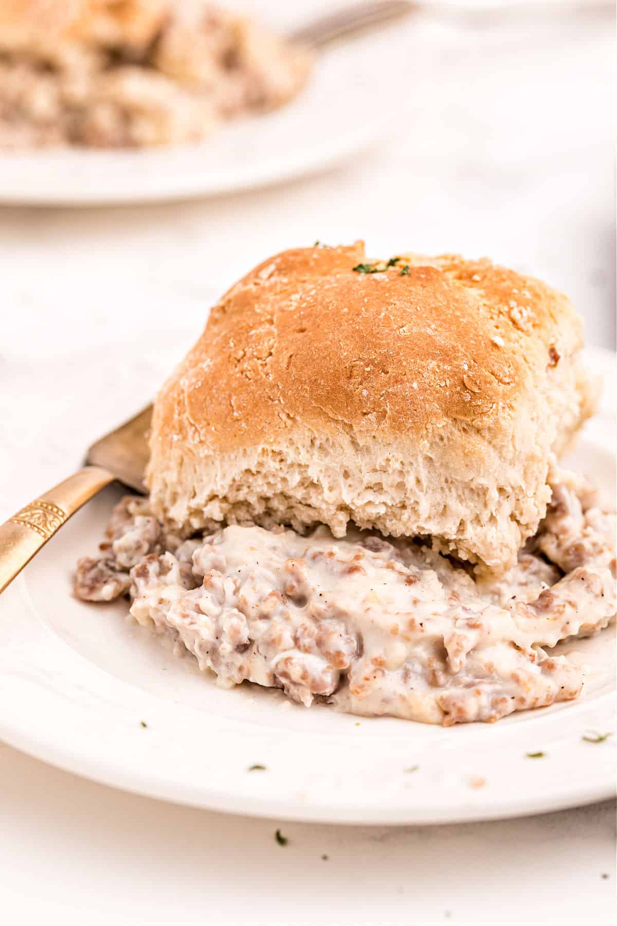 Sausage and gravy with biscuit served on a white plate.