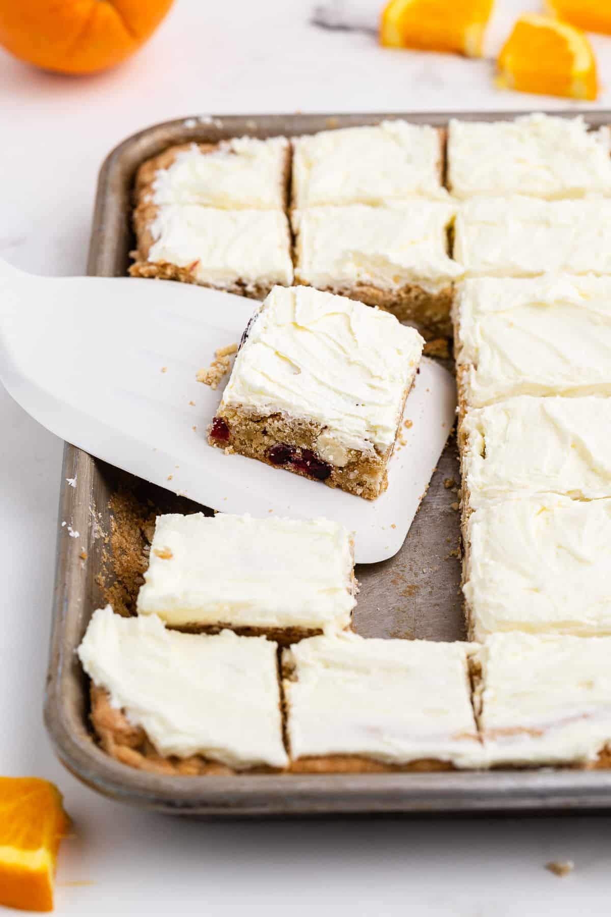 Cranberry orange cookie bars cut into squares and topped with frosting.