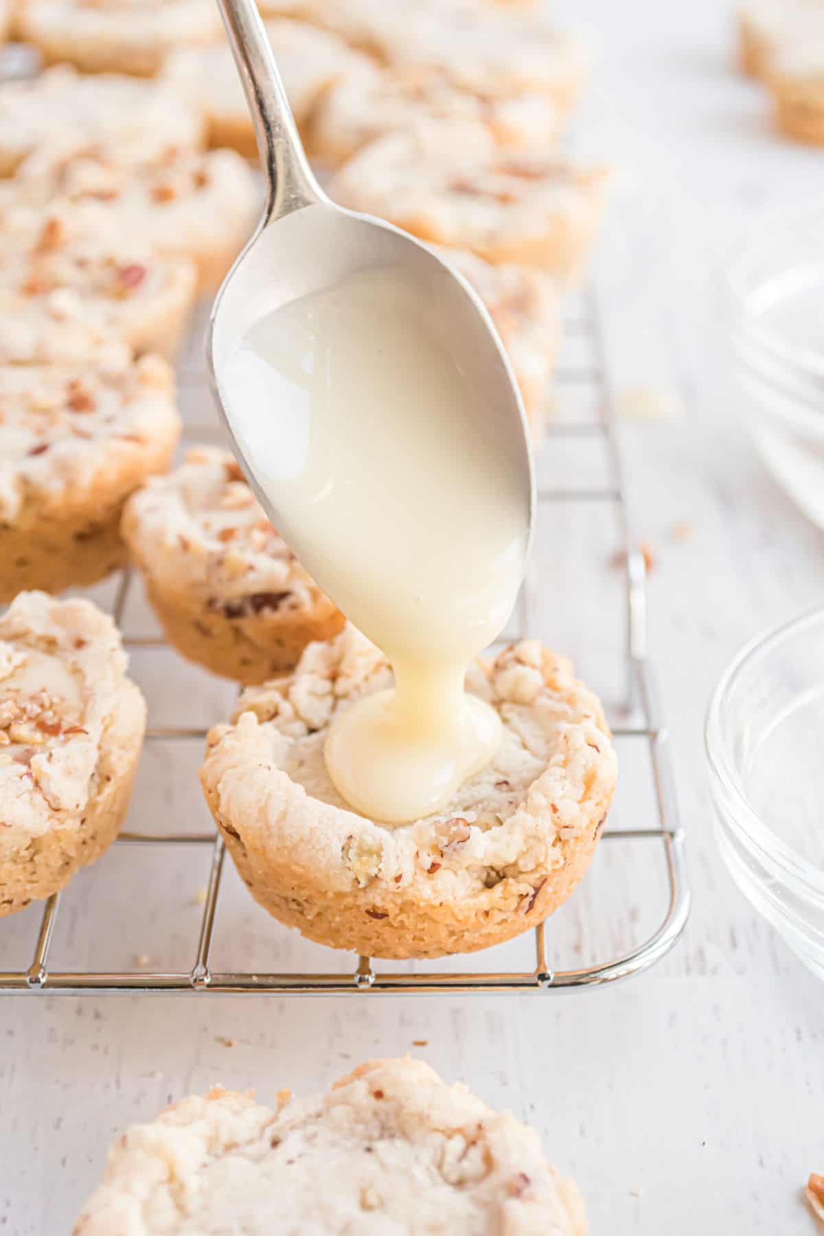 Pecan cookies on a wire rack with a spoon drizzling eggnog glaze on top.