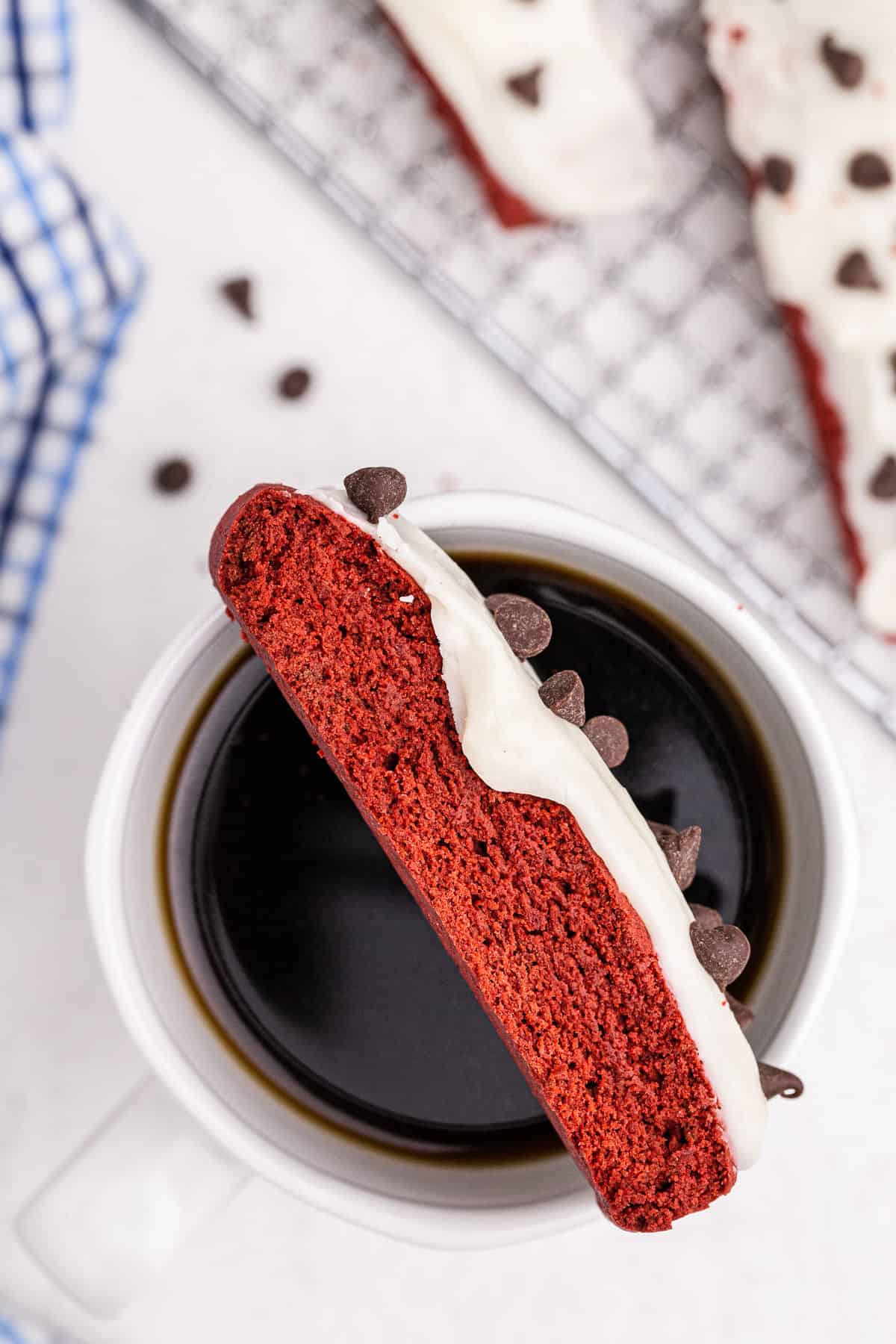 red velvet biscotti with vanilla icing on a mug of coffee.