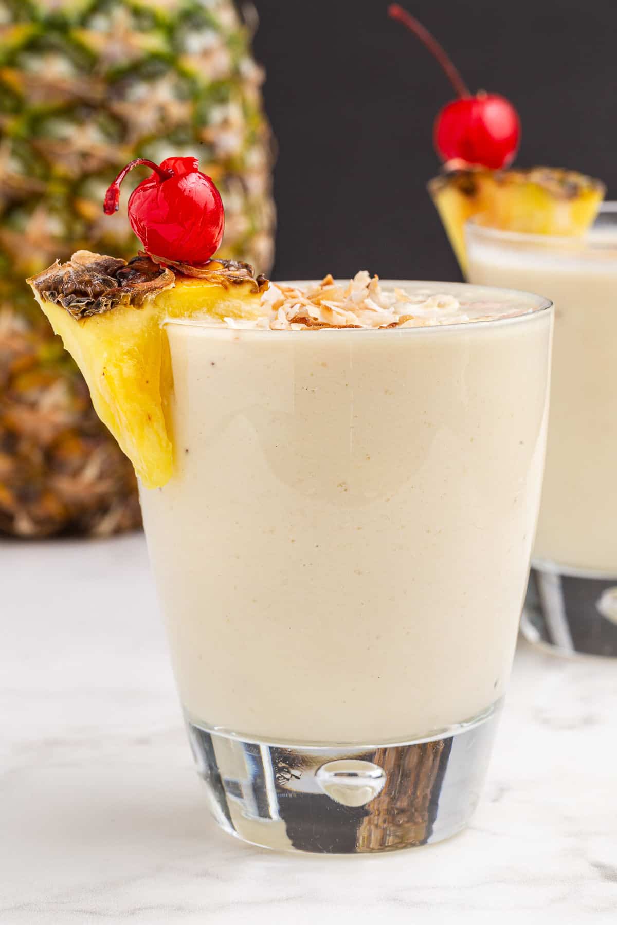 Pina colada smoothie in a clear glass with pineapple garnish.