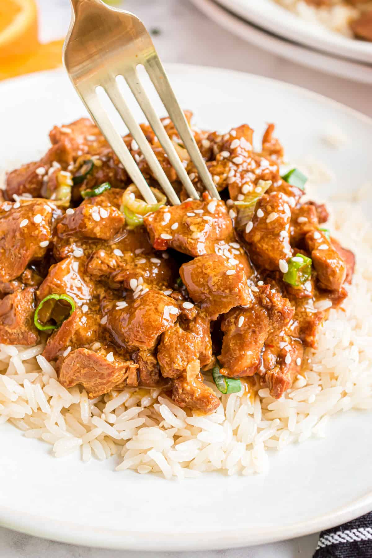 Orange chicken served over rice on a white plate.