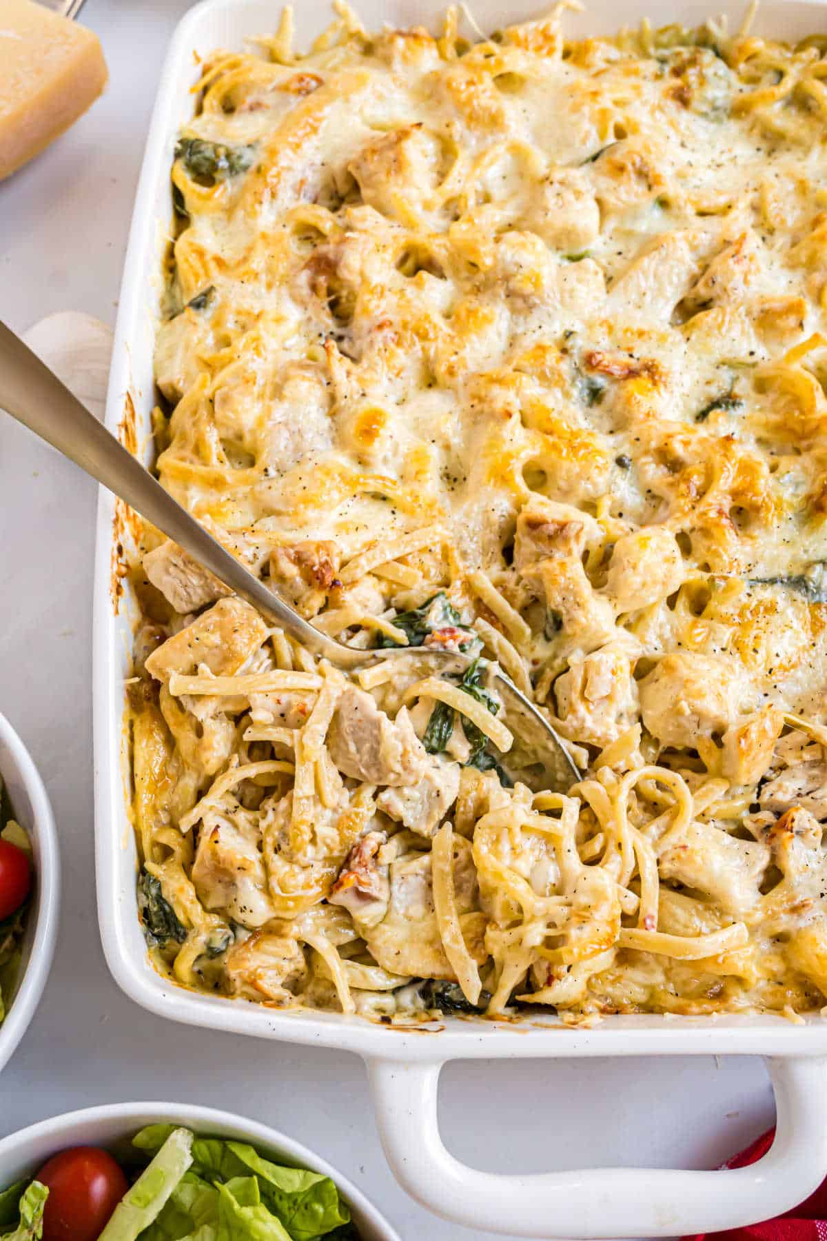 Italian chicken casserole baked pasta with melted cheese on top, served in a white dish with a serving spoon.