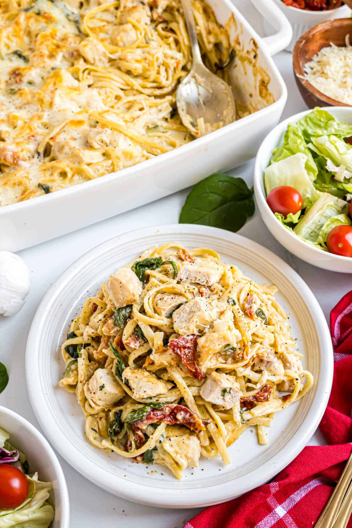 Plate of creamy pasta with chicken, sun-dried tomatoes, and spinach served alongside a fresh salad and hearty Italian chicken casserole.