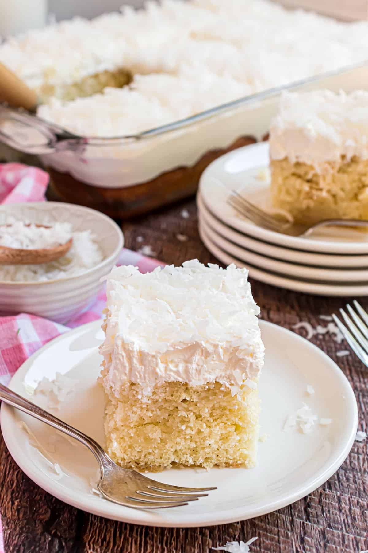 Slice of coconut cream poke cake on a white plate with fork.