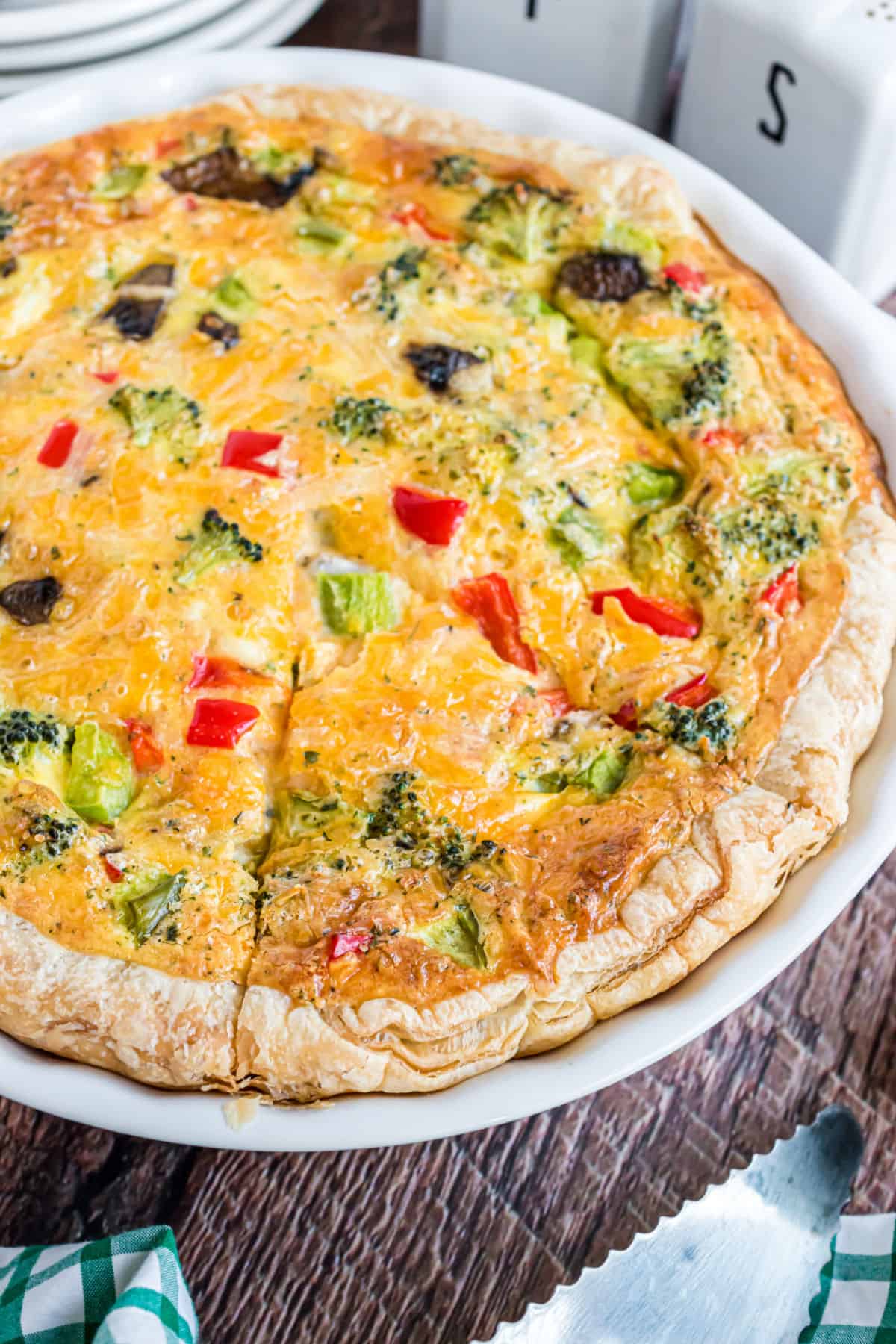 Veggie quiche in pie plate with slices cut.