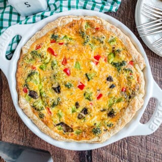 Vegetable quiche in a white pie plate filled with veggies and cheese.