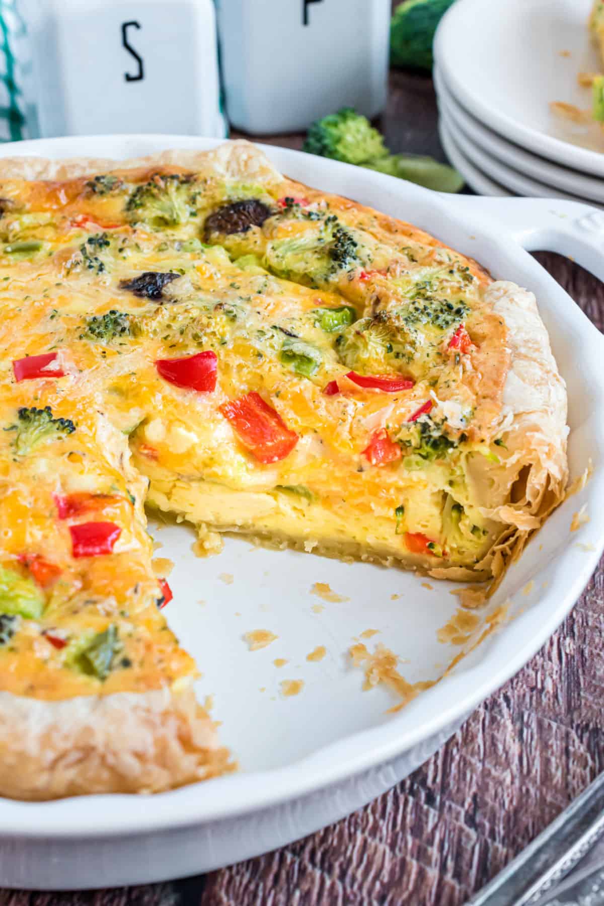 Veggie quiche in pie plate with one slice removed.