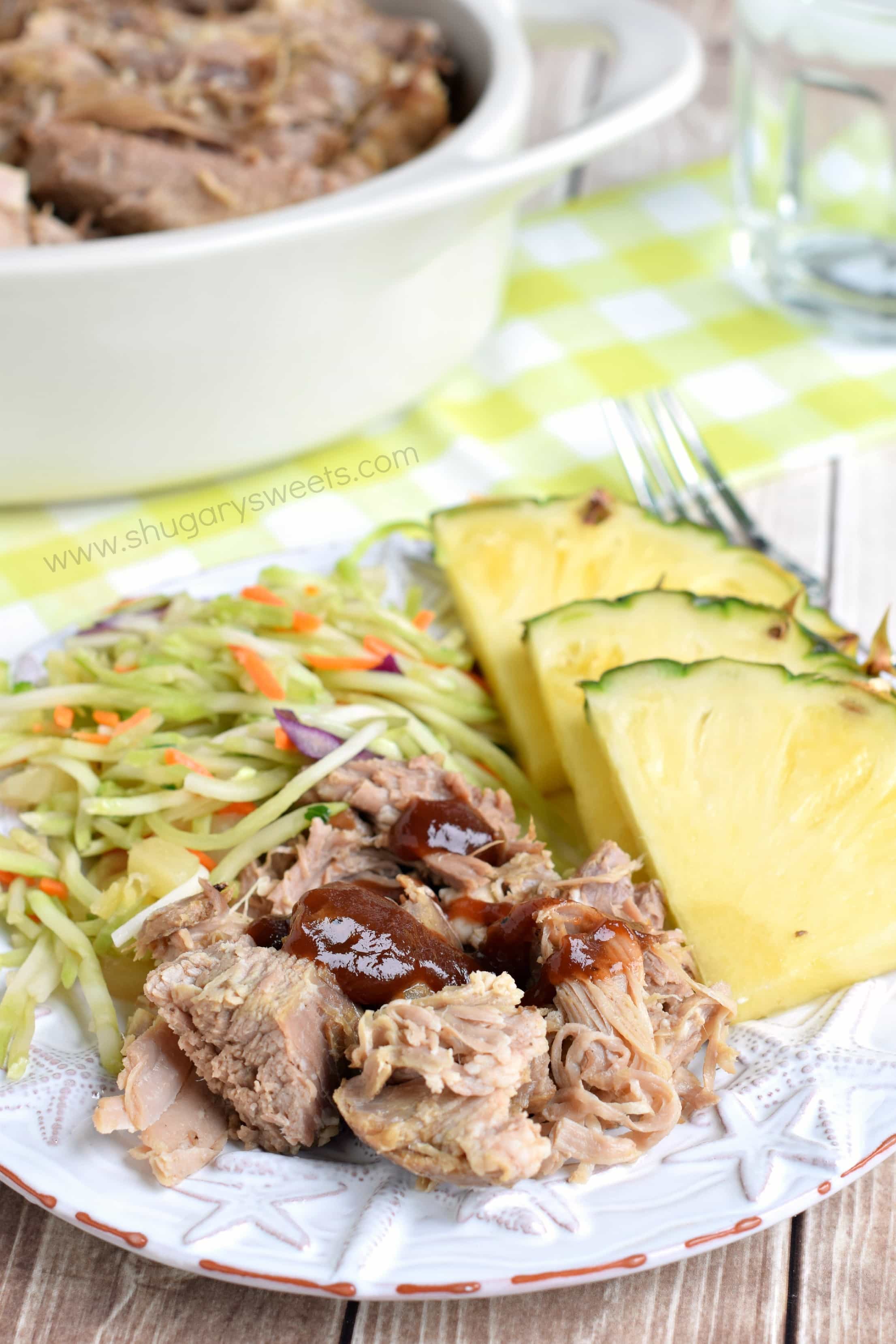 Kalua pork on a dinner plate with slaw and pineapple.