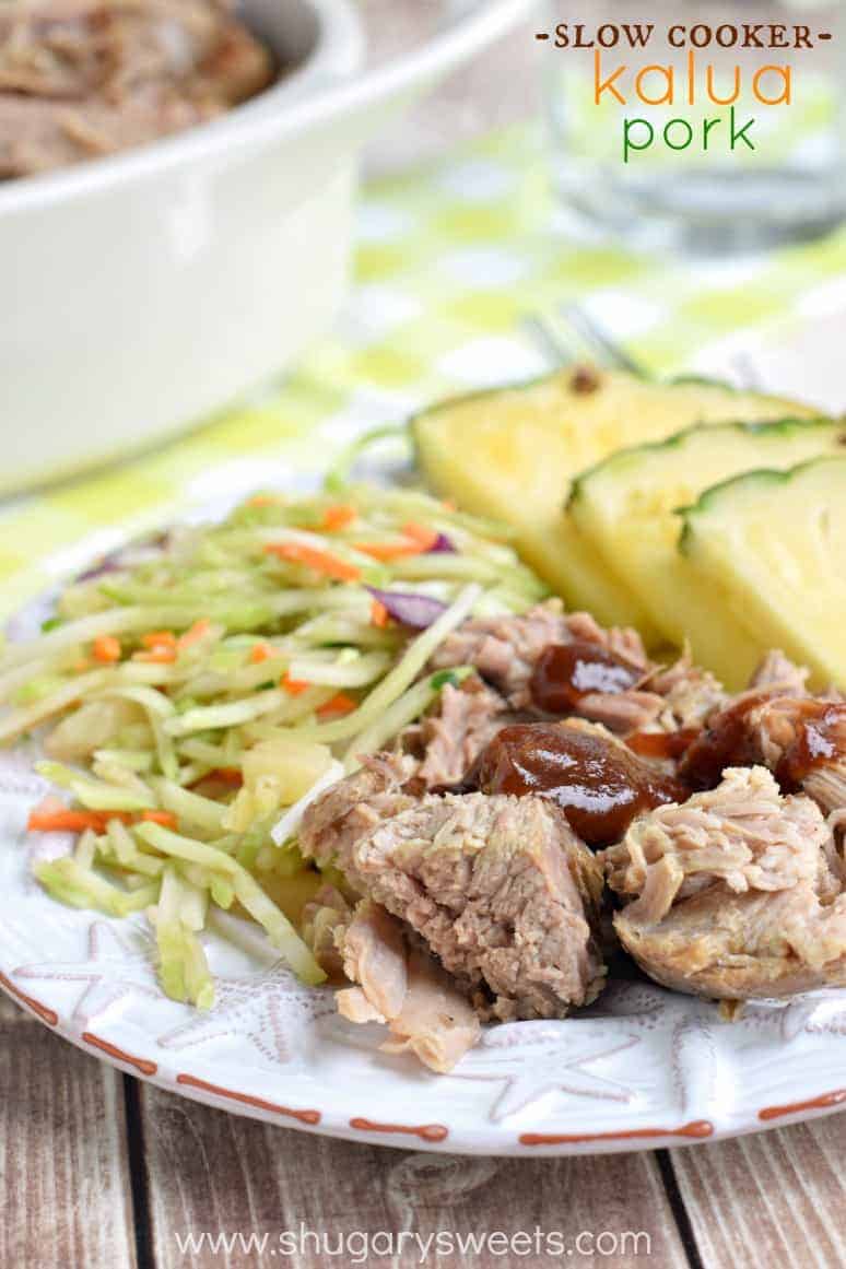 Chunks of tender kalua pork on a white plate with bbq sauce, hawaiian slaw, and fresh pineapple.