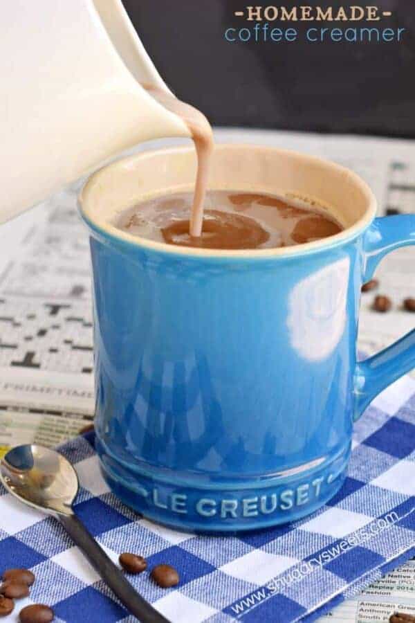 Blue mug of coffee with creamer being added.
