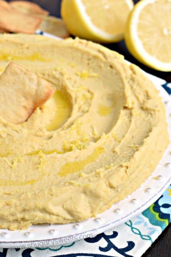 Creamy swirls of lemon hummus on a plate drizzled with olive oil and topped with lemon zest.