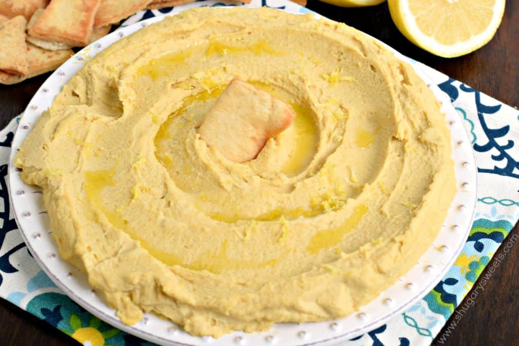 Lemon hummus on a white plate served with pita chips.