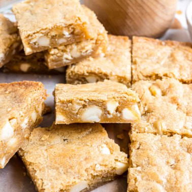 Golden brown macadamia nut blondies with white chocolate chips, cut into squares and stacked on parchment paper.