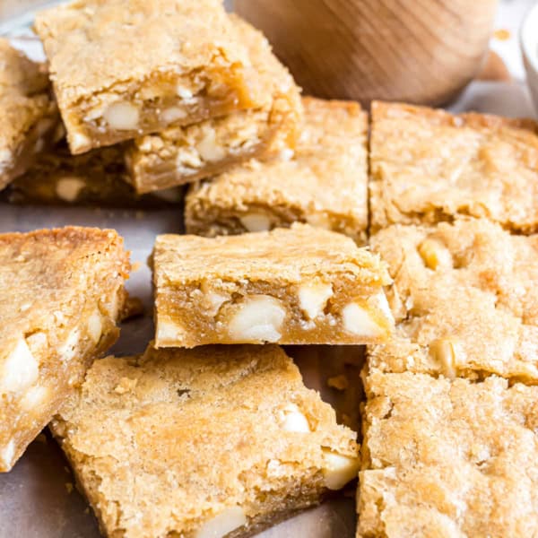 Golden brown macadamia nut blondies with white chocolate chips, cut into squares and stacked on parchment paper.