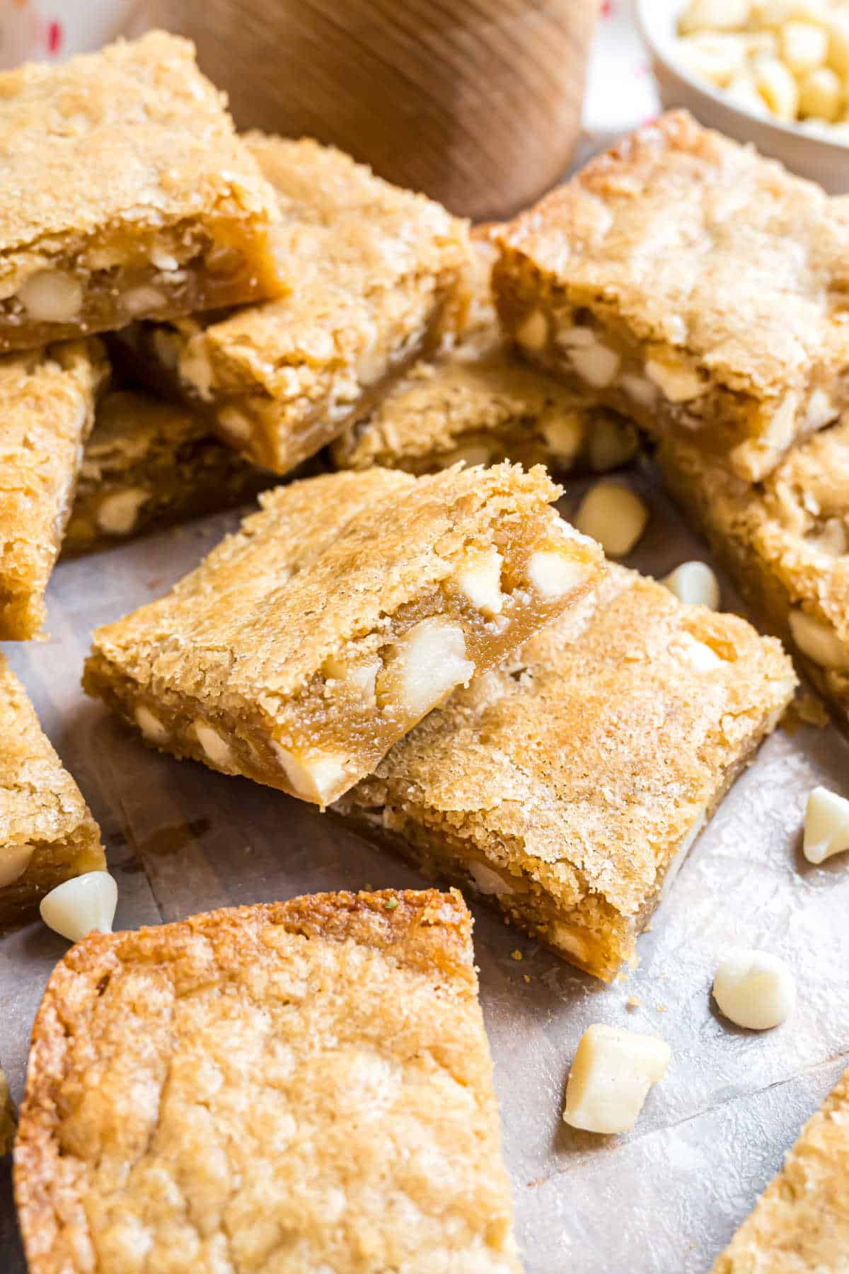 Macadamia nut blondies with white chocolate chips are stacked on a parchment-lined surface, highlighting their rich, chewy texture and irresistible flavor.