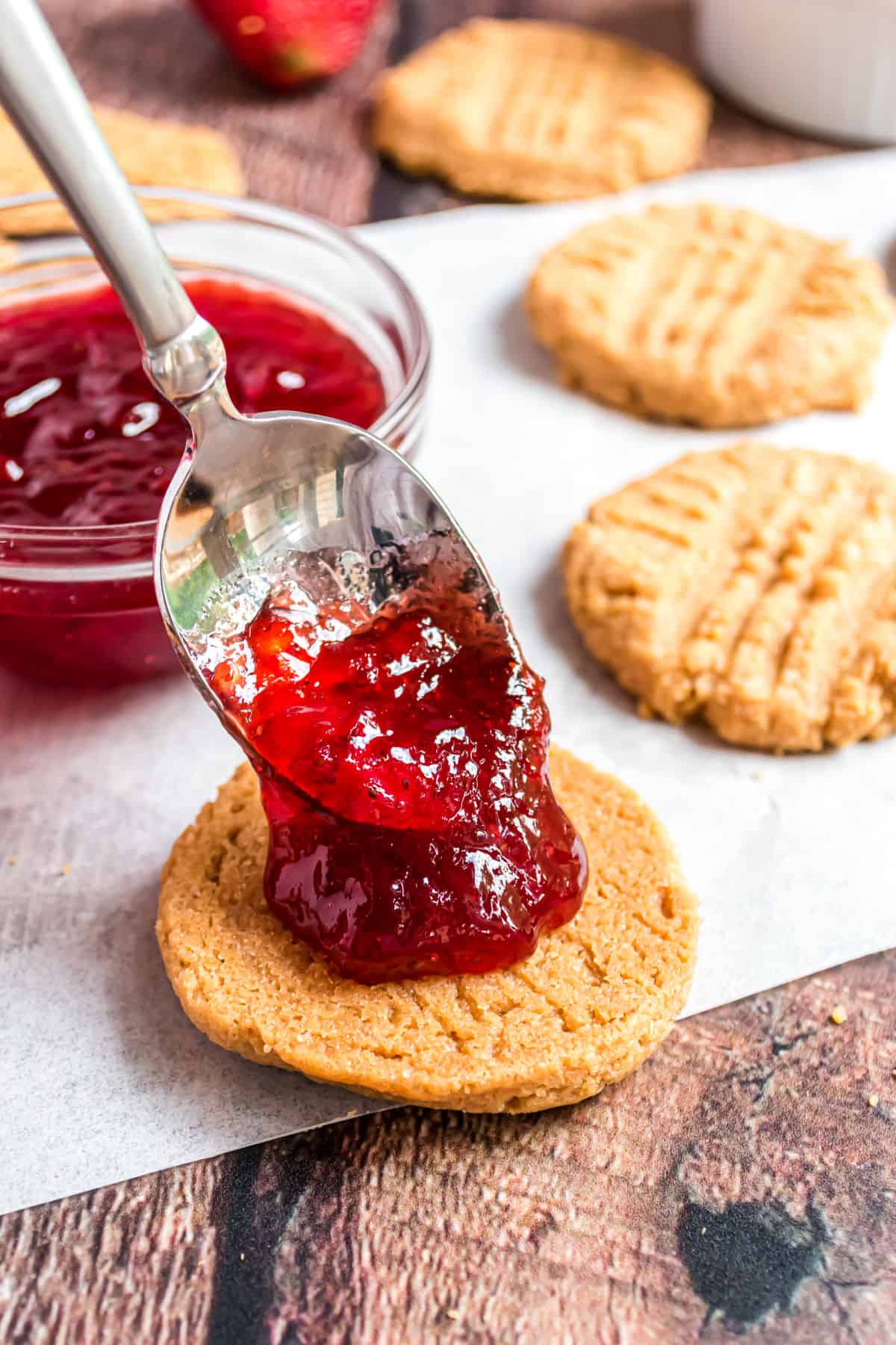 Strawberry preserves being spooned onto a peanut butter cookie to make a cookie sandwich.