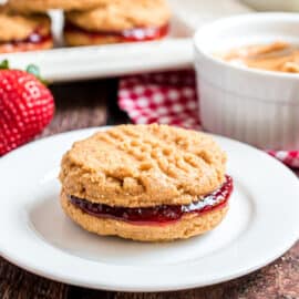 Peanut butter sandwich cookie with strawberry filling on white plate.
