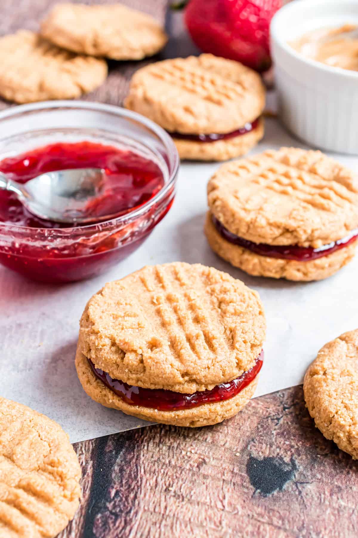 Baked peanut butter cookies with strawberry preserves filling on parchment paper.