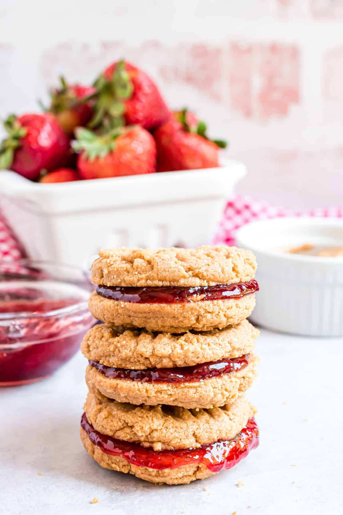 Stack of three pb&j cookies with a bowl of strawberries in background.