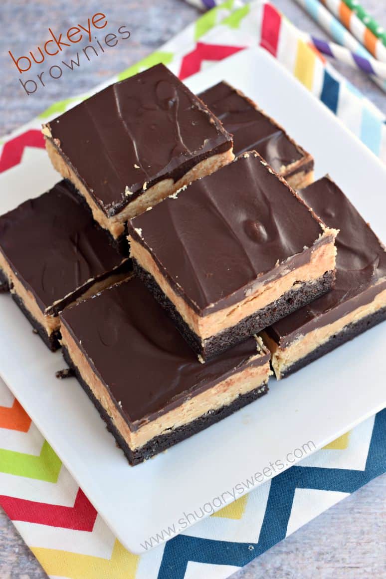 Brownies topped with peanut butter filling and chocolate ganache cut into squares and stacked on a white plate.