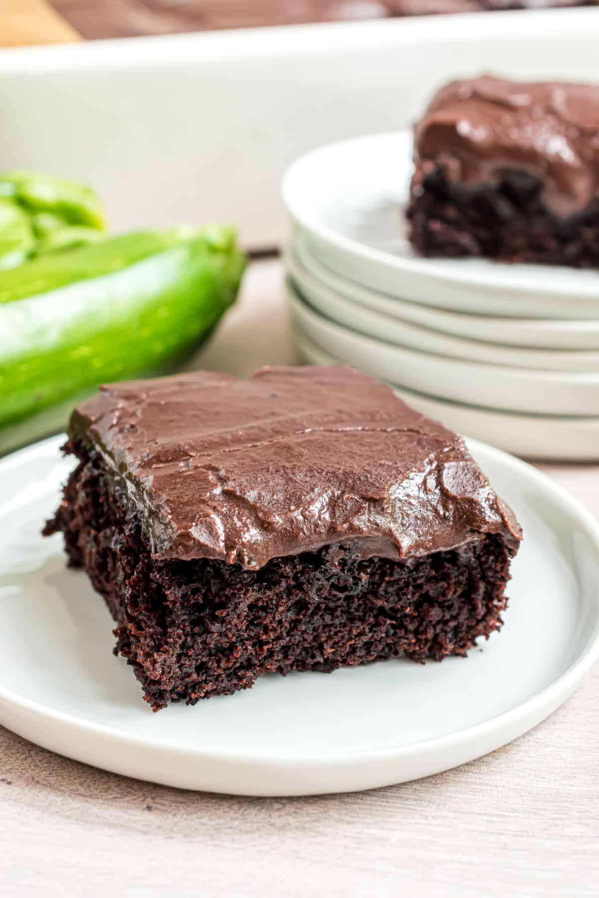 Slices of chocolate frosted zucchini brownies on white dessert plates.