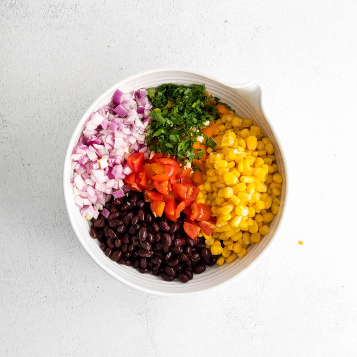 Ingredients for corn and black bean salsa in a white bowl.